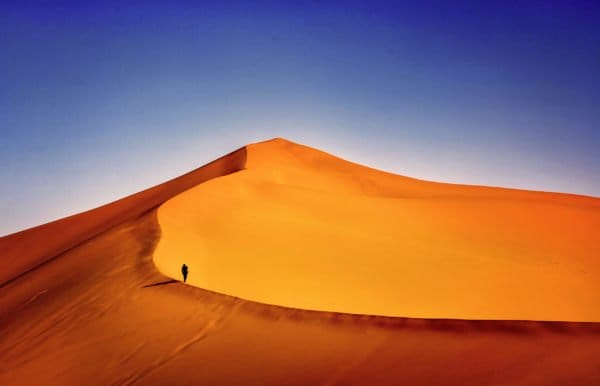 A large sand dune with a solo person climbing it