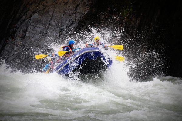 Raft breaking through wave on river with paddlers