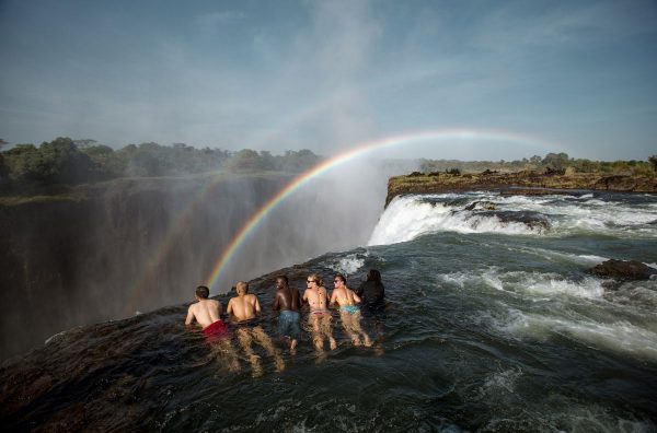 Incredible things to do before rafting the Zambezi: bathe in the devil's pool at the crest of Victoria Falls. Image shows a group of five people lying at the lip of the falls looking over the edge