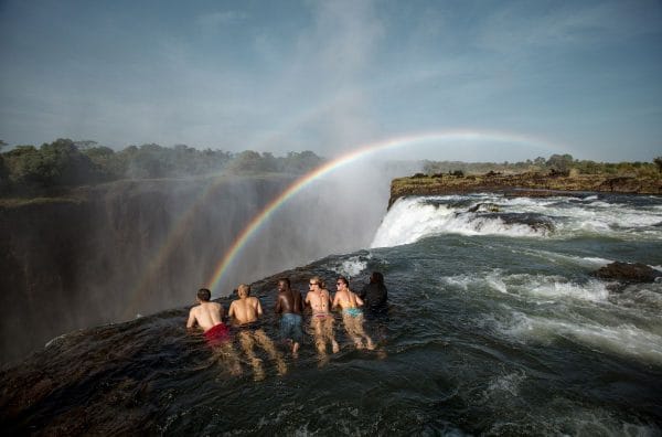 Incredible things to do before rafting the Zambezi: bathe in the devil's pool at the crest of Victoria Falls. Image shows a group of five people lying at the lip of the falls looking over the edge