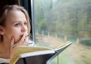 Beat the post holiday blues by writing a diary. Girl writing journal while travelling by train